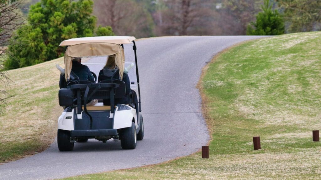 Two people in golf cart driving down paved trail